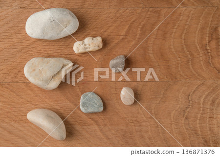 Smooth stones, of various sizes, are scattered on a wooden board 136871376