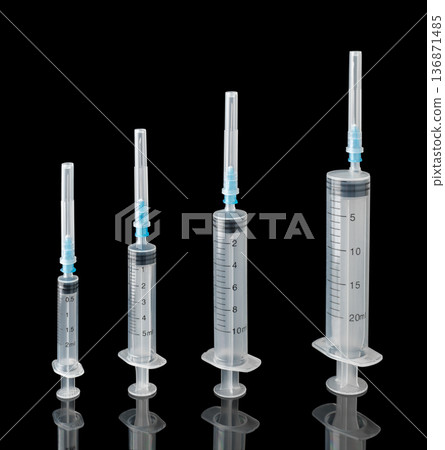 Four disposable syringes with sealed needles on a black background with reflection 136871485