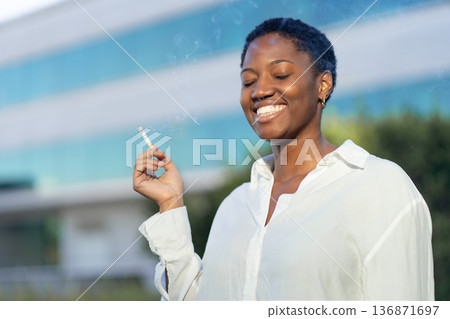 Smiling businesswoman smoking against modern Smiling businesswoman smoking against modern 136871697