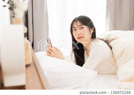 A woman using a smartphone while lying in bed A woman using a smartphone while lying in bed 136872288