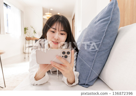 一個女人躺在沙發上,看著她的智能手機 一個女人躺在沙發上,看著她的智能手機 136872396