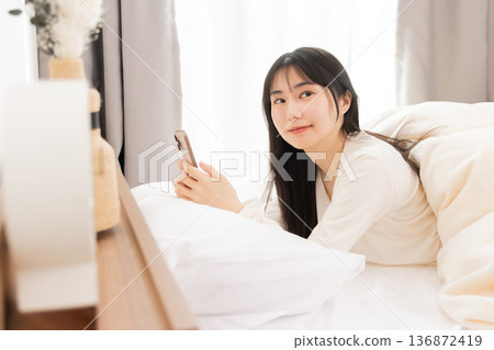 A woman using a smartphone while lying in bed 136872419