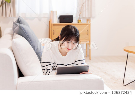 A woman lying on a sofa looking at a tablet PC A woman lying on a sofa looking at a tablet PC 136872424