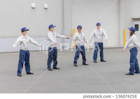 A group of workers doing exercises in front of a factory A group of workers doing exercises in front of a factory 136874258