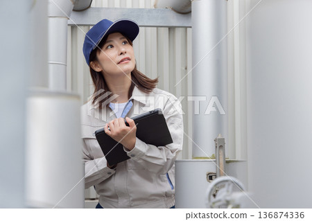 A female worker inspecting outdoor machinery 136874336