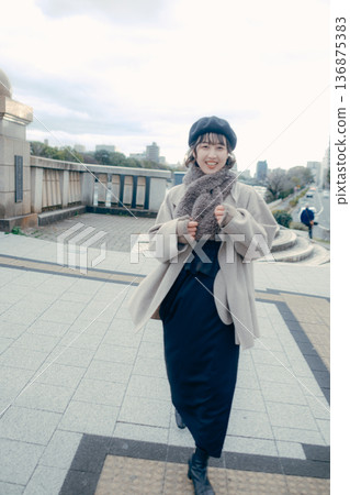 一位三十多歲的日本女性微笑著走在冬日的城市街道上。 136875383