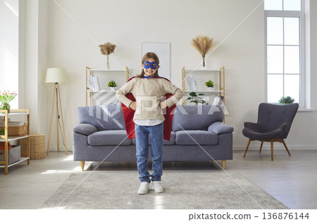 Child in super hero costume standing in the living room at home and looking cheerful at camera. Child in super hero costume standing in the living room at home and looking cheerful at camera. 136876144