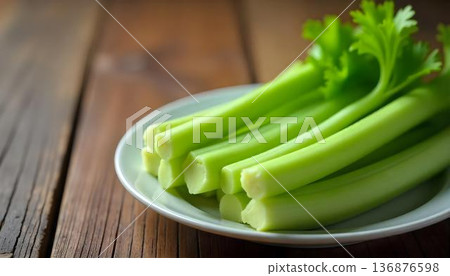 Fresh celery arranged on a white plate atop a wooden table, celebrating National Celery Month and healthy snacking 136876598