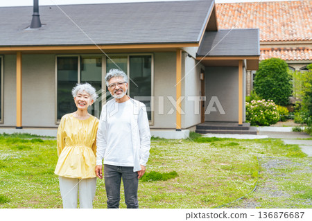 Smiling senior couple standing in front of their house Smiling senior couple standing in front of their house 136876687