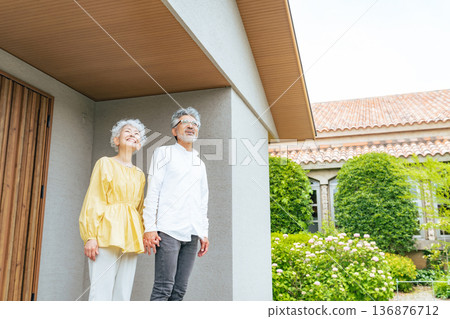 Smiling senior couple standing in front of their house Smiling senior couple standing in front of their house 136876712