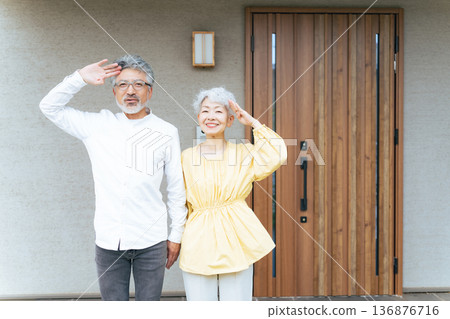 Smiling senior couple standing in front of their house Smiling senior couple standing in front of their house 136876716