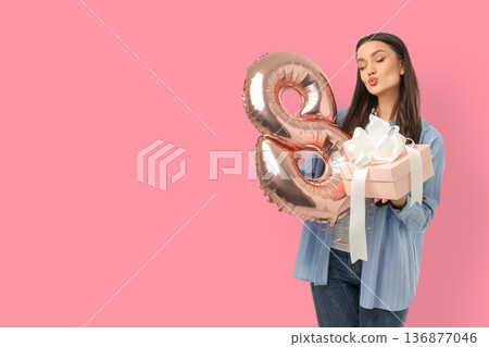 A young woman holds a present and a balloon showing the number 8 A young woman holds a present and a balloon showing the number 8 136877046