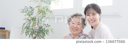 特寫鏡頭：一位微笑的孫子和年邁的祖母並肩站著，看向鏡頭，橫幅象徵著關懷和親子關係。 136877088