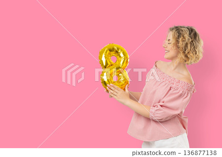 A woman holds a golden balloon shaped like the number 8 A woman holds a golden balloon shaped like the number 8 136877138