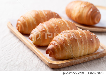 Salt bread (Shio pan) with sea salt flakes on a wooden plate with white fabric background Salt bread (Shio pan) with sea salt flakes on a wooden plate with white fabric background 136877870