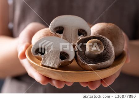 Hands holding wooden plate of fresh crimini mushroom or baby bella mushroom Hands holding wooden plate of fresh crimini mushroom or baby bella mushroom 136877890