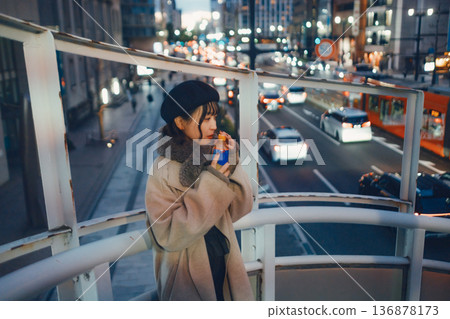 一位三十多歲的日本女性在夜色下的城市裡手持一杯熱飲。 136878173