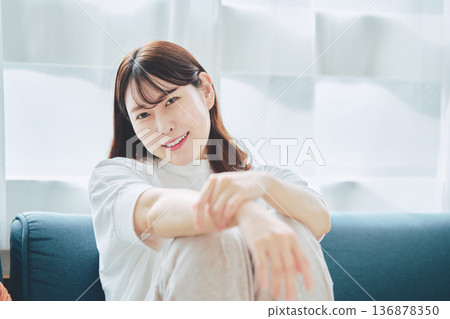 Portrait of a smiling woman in her 30s relaxing in a living room with natural light Portrait of a smiling woman in her 30s relaxing in a living room with natural light 136878350