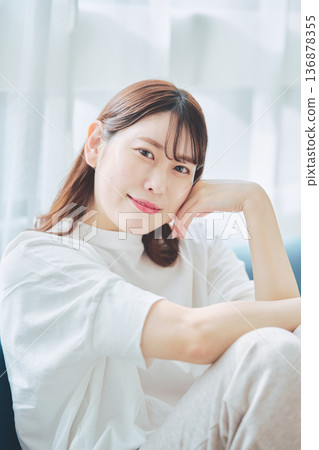 Portrait of a smiling woman in her 30s relaxing in a living room with natural light Portrait of a smiling woman in her 30s relaxing in a living room with natural light 136878355