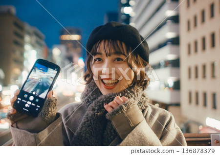 一位微笑的日本女子在夜晚的城市使用智慧型手機。 136878379