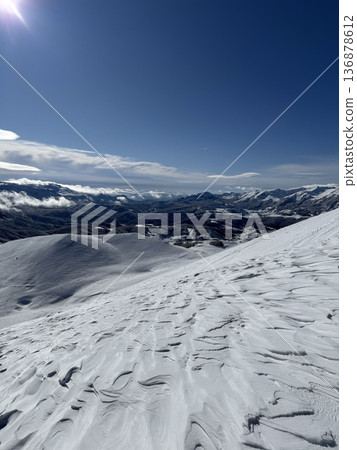 Snow-covered mountain slope and wide winter landscape under clear blue sky with sunlight and distant peaks Snow-covered mountain slope and wide winter landscape under clear blue sky with sunlight and distant peaks 136878612