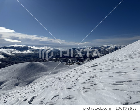 Snow-covered mountain slope and panoramic alpine landscape under clear blue winter sky 136878613