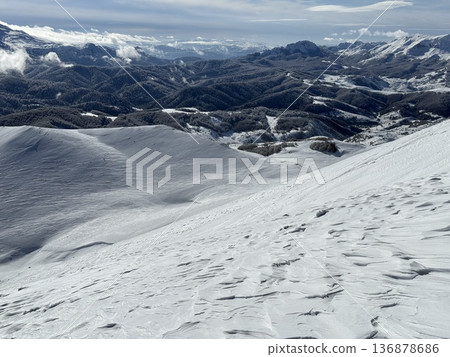 Snowy mountain landscape with rolling winter hills and distant forested ridges under blue sky Snowy mountain landscape with rolling winter hills and distant forested ridges under blue sky 136878686