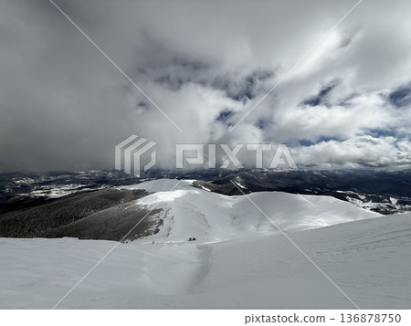 Snow-covered mountain summit under dramatic winter clouds with panoramic alpine landscape Snow-covered mountain summit under dramatic winter clouds with panoramic alpine landscape 136878750