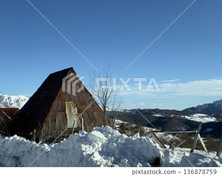 Rustic triangular barn in snow with mountain landscape under clear blue winter sky 136878759