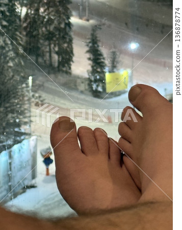 Relaxing by a snowy ski slope with bare feet up against a window at night 136878774