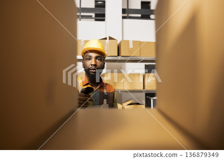 Black employee using a barcode scanner to update inventory system, managing products for e-business shipments, parcel express deliveries and retail order processing. Quality control. 136879349