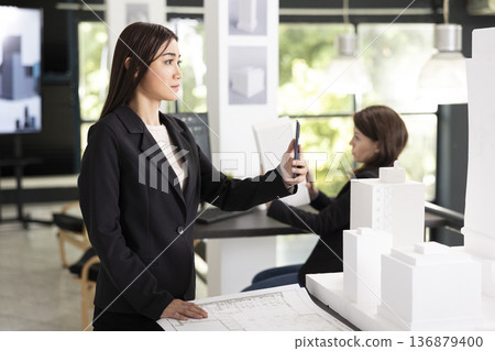 Young architect uses cellphone to communicate with contractors, providing updates on building design. Female designer with scale model on table, joins video call with client to share project progress Young architect uses cellphone to communicate with contractors, providing updates on building design. Female designer with scale model on table, joins video call with client to share project progress 136879400
