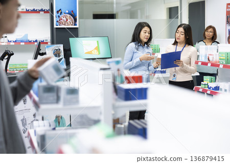 Asian drugstore attendant explains prescription and health insurance details to female customer in modern pharmacy. Informative consultation emphasizes healthcare support and patient understanding. Asian drugstore attendant explains prescription and health insurance details to female customer in modern pharmacy. Informative consultation emphasizes healthcare support and patient understanding. 136879415