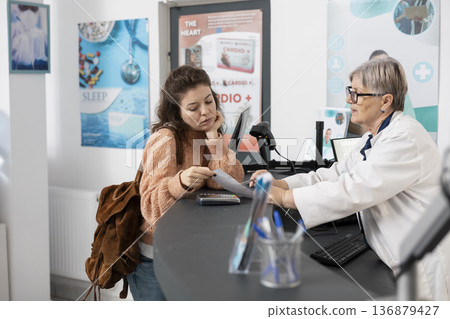 Female customer reviews prescription with pharmacist, carefully confirming medication details during professional consultation. White woman checks drugstore receipt to ensure accuracy in purchase. Female customer reviews prescription with pharmacist, carefully confirming medication details during professional consultation. White woman checks drugstore receipt to ensure accuracy in purchase. 136879427