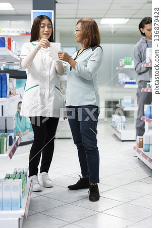 Female drugstore attendant advises middle aged woman on medication and health supplements in local dispensary. Professional consultation highlights patient care, trust and attentive customer service Female drugstore attendant advises middle aged woman on medication and health supplements in local dispensary. Professional consultation highlights patient care, trust and attentive customer service 136879428