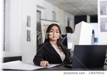 Female architectural designer reviewing blueprints and researching building concepts. Woman architect focuses on planning tasks, organizing timelines and preparing reports for company projects. 136879542