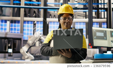 Engineer performing predictive maintenance using laptop, analyzing IoT sensor data, managing operational reliability of photovoltaic systems in smart factory environment, camera B Engineer performing predictive maintenance using laptop, analyzing IoT sensor data, managing operational reliability of photovoltaic systems in smart factory environment, camera B 136879596