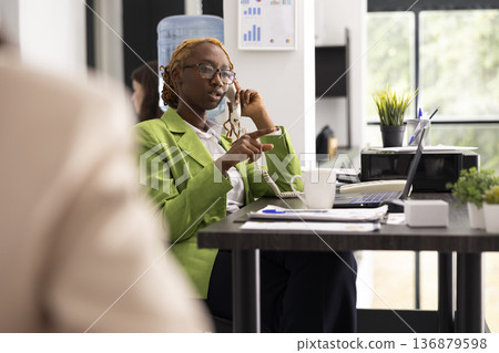 Focused analyst manages business call on landline phone, providing information and clarifying project details. Serious consultant negotiates with client on telephone, discussing company proposal. 136879598