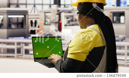 Factory engineer typing on green screen laptop, monitoring production lines. Woman in industry 4.0 plant ensures machinery operates at optimal efficiency using chroma key mockup notebook, camera B Factory engineer typing on green screen laptop, monitoring production lines. Woman in industry 4.0 plant ensures machinery operates at optimal efficiency using chroma key mockup notebook, camera B 136879599