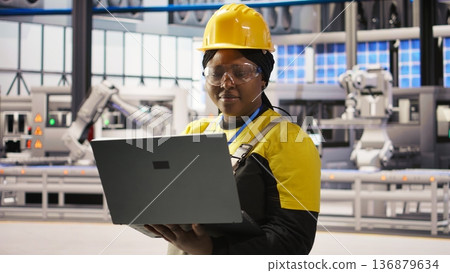 Solar panels factory engineer analyzing data from IoT sensors to refine equipment operational efficiency. Worker performing system diagnostics to reduce downtime in photovoltaic production, camera A 136879634