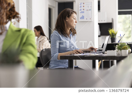 Skilled female consultant using laptop to review business information and draft project updates. Focused white woman diligently working on company annual report and preparing presentations. 136879724