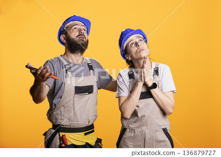 Construction partners glance upward with dramatic frustration, facing renovation setbacks. Renovators pleading for good news during unpredictable challenges of building, repairs and DIY projects. 136879727