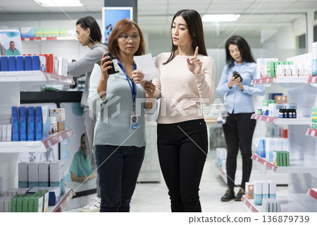 Female pharmacy employee discusses prescription details and health supplements with middle aged customer in modern drugstore. Focus on medical consultation, healthcare advice and patient support. 136879739