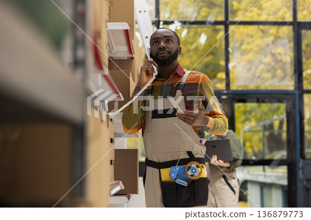 African american male on a landline phone call coordinates dispatch services, ensuring quality control in parcel preparation and express delivery for retail and e-business shipments. African american male on a landline phone call coordinates dispatch services, ensuring quality control in parcel preparation and express delivery for retail and e-business shipments. 136879773