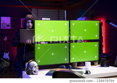 Hacker in office using laptop and exploits on isolated screen PC to break into systems and access restricted data. Man using mockup multi monitor setup VPN on dark web to sell sensitive information 136879784