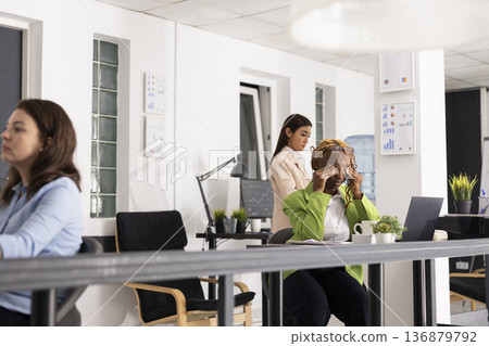 Overworked female employee rubbing eyes in pain, showing stress and mental fatigue from demanding corporate workday. African American employee sits stressed at laptop, trying to regain focus. Overworked female employee rubbing eyes in pain, showing stress and mental fatigue from demanding corporate workday. African American employee sits stressed at laptop, trying to regain focus. 136879792