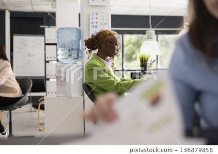 Diligent businesswoman sits at desk planning marketing strategy and preparing for upcoming presentation. Black female employee organizes daily tasks, contributing to productive and diverse workplace. Diligent businesswoman sits at desk planning marketing strategy and preparing for upcoming presentation. Black female employee organizes daily tasks, contributing to productive and diverse workplace. 136879858