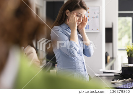 Stressed professional woman touches head in frustration and analyzes marketing strategy files on digital device. Tired employee experiences pressure and anxiety in busy workplace. Stressed professional woman touches head in frustration and analyzes marketing strategy files on digital device. Tired employee experiences pressure and anxiety in busy workplace. 136879860
