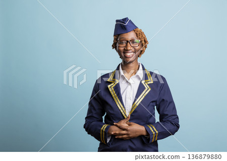 Friendly black woman in flight attendant uniform looking at camera with radiant smile against isolated background. African american air hostess posing for professional airline company portrait. Friendly black woman in flight attendant uniform looking at camera with radiant smile against isolated background. African american air hostess posing for professional airline company portrait. 136879880