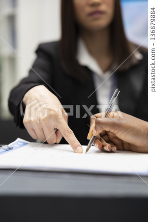 Female receptionist points at clipboard while assisting black patient signing medical insurance forms at hospital front desk. Healthcare staff member provides guidance with registration and paperwork. Female receptionist points at clipboard while assisting black patient signing medical insurance forms at hospital front desk. Healthcare staff member provides guidance with registration and paperwork. 136879884